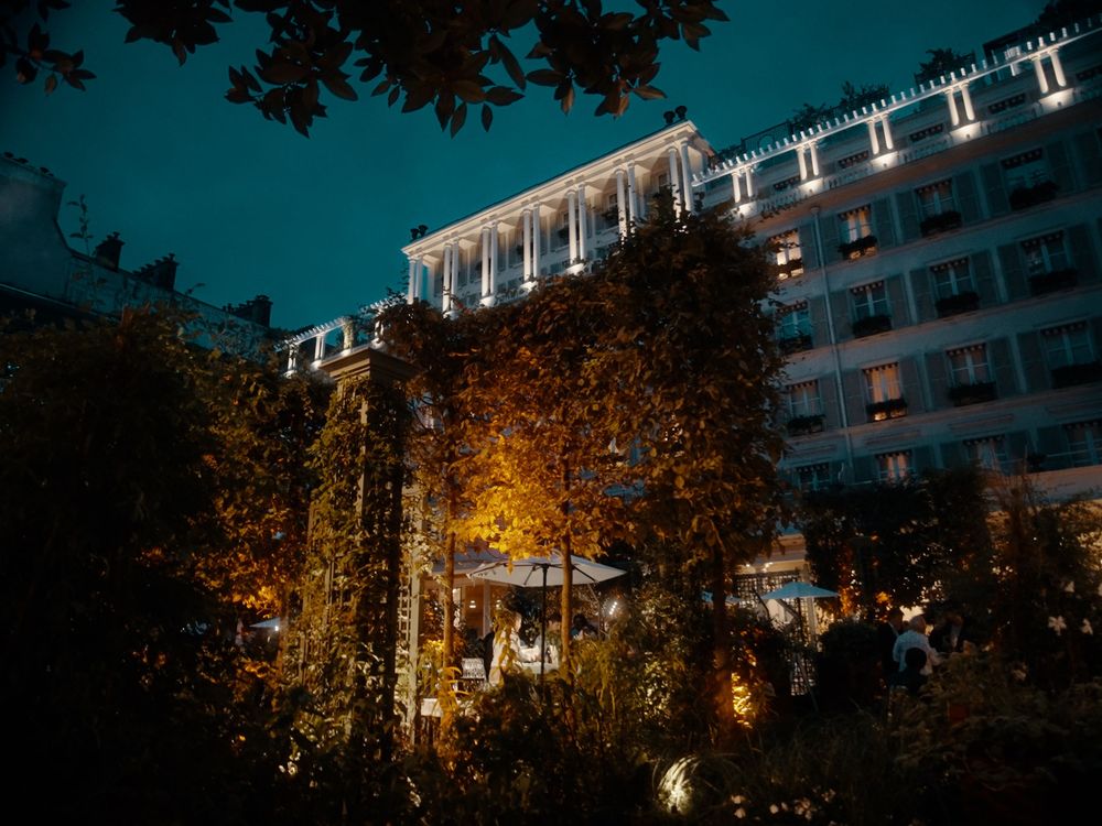 Modern apartment buildings illuminated at night with trees silhouetted against a dark blue sky.