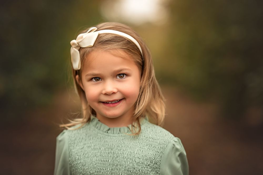 A child wearing a sage green sweater poses in a series of natural light portraits with a soft bokeh background.