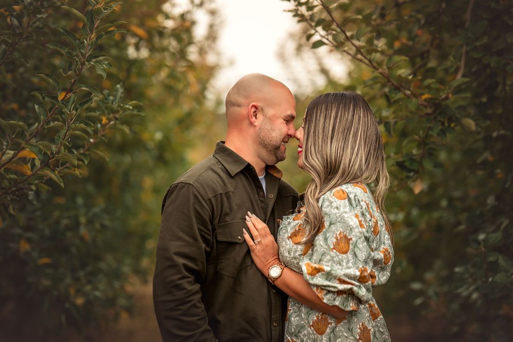Romantic couple embraces in a lush garden setting during golden hour with autumn foliage in background.