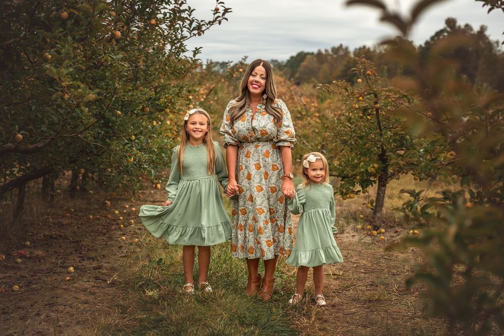 Children and adults in matching mint green and floral dresses walk through an autumn forest setting at golden hour.