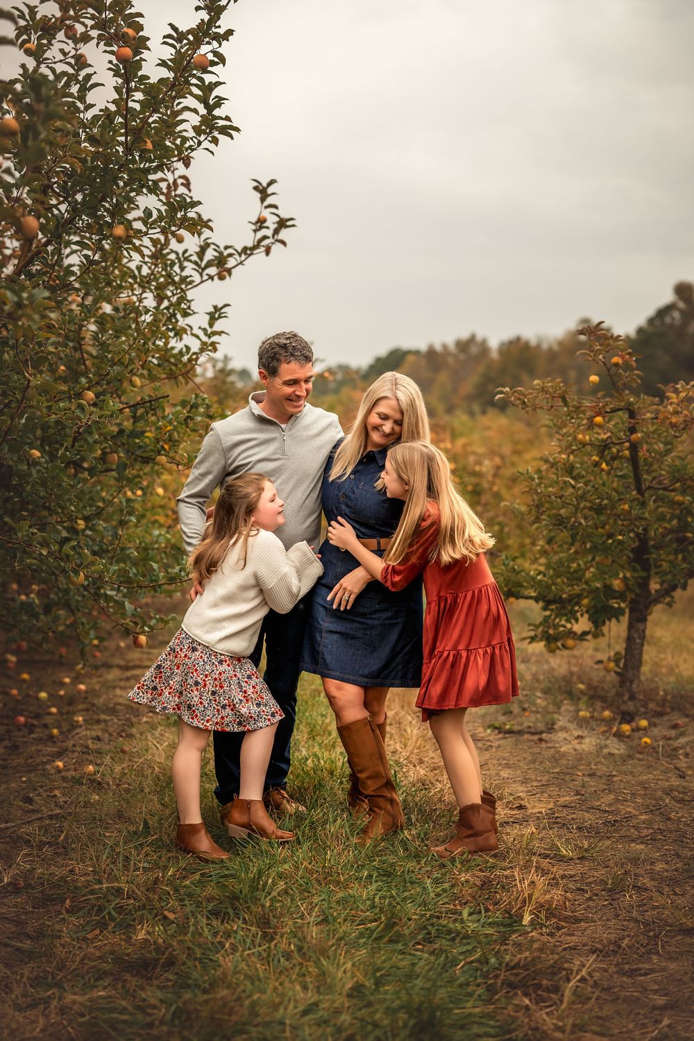 A family shares playful moments together while walking through an apple orchard on a fall day.