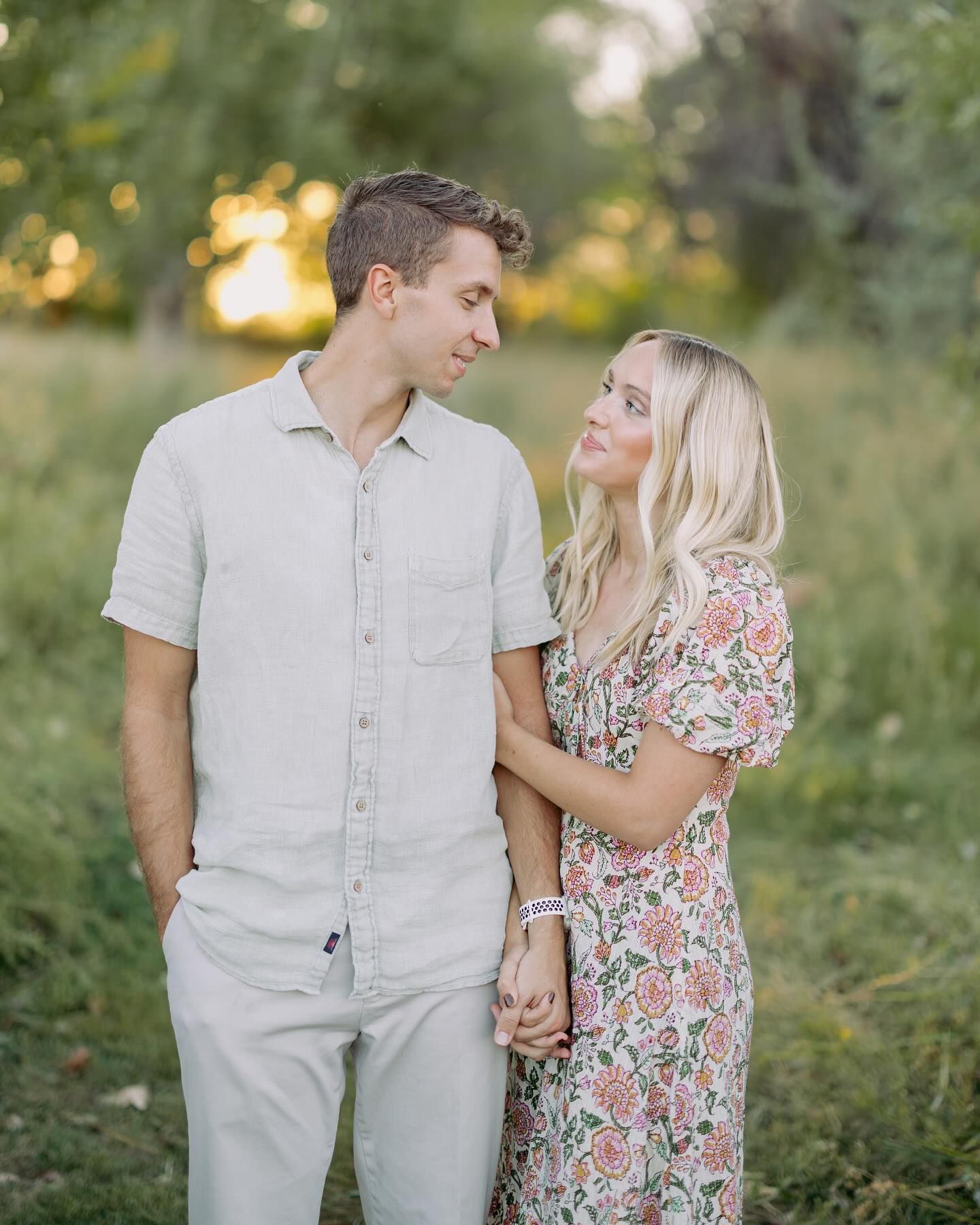 A couple in light summer attire shares intimate moments while walking through a lush garden setting at sunset.