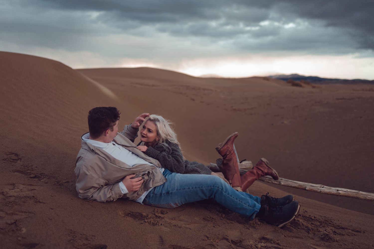 spring beach engagement session, couple lay comfortably in the dunes, with a moody sky in the background.