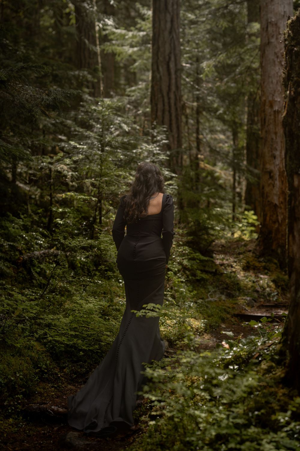 A figure in a black dress walks through a mystical forest path.