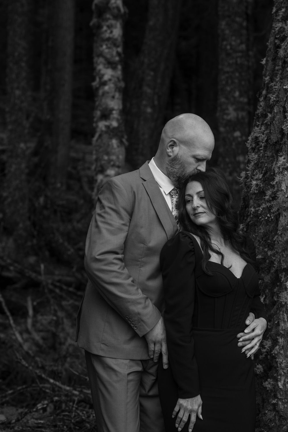 A romantic moment captured in a moody forest setting with dramatic black and white photography.