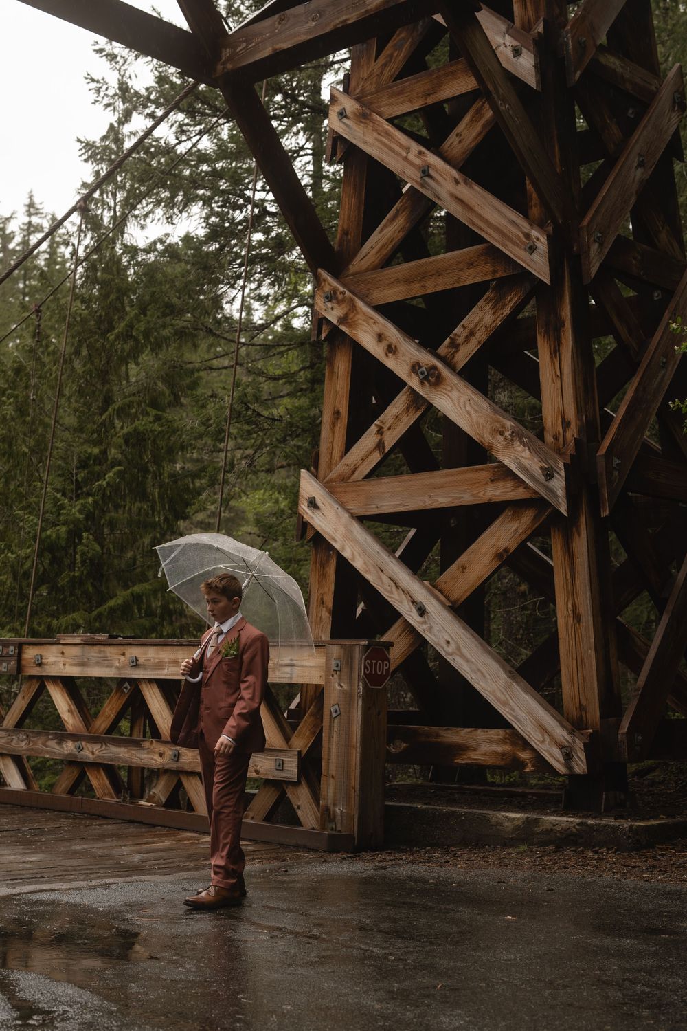 Wooden boots and legs stand on a rustic covered bridge during a rainy day in the forest.