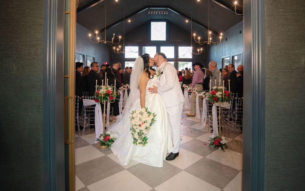 A bride and groom walk down a dimly lit hallway with elegant chandeliers overhead during their wedding reception.