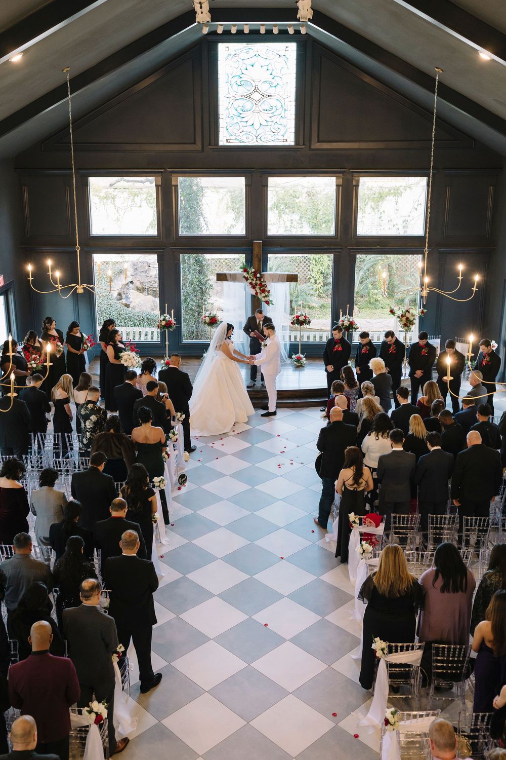 A panoramic view of an indoor wedding ceremony in a modern venue with black and white checkered flooring and high ceilings.