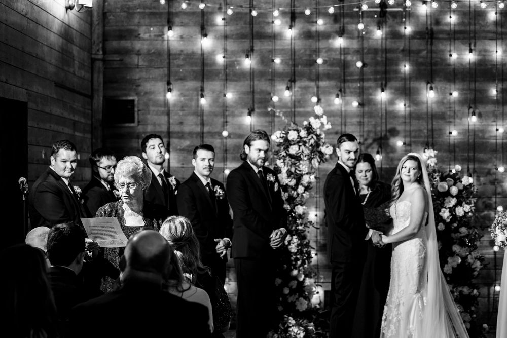 A romantic wedding reception under glowing string lights with guests dancing and celebrating in an elegant indoor venue.
