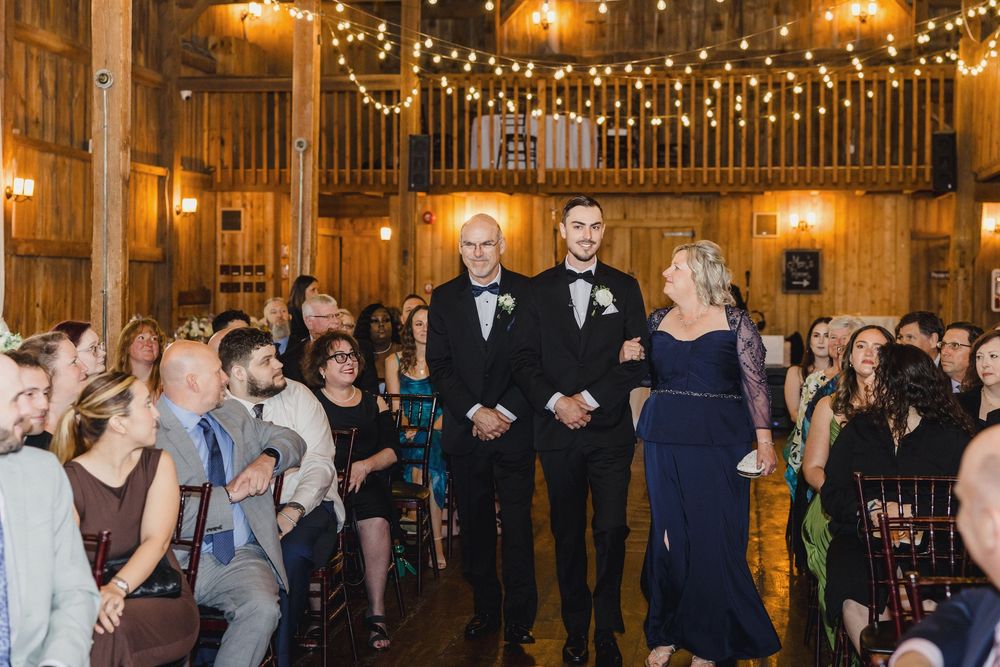 Wedding guests dance and celebrate under warm string lights in a rustic wooden barn venue during the reception.