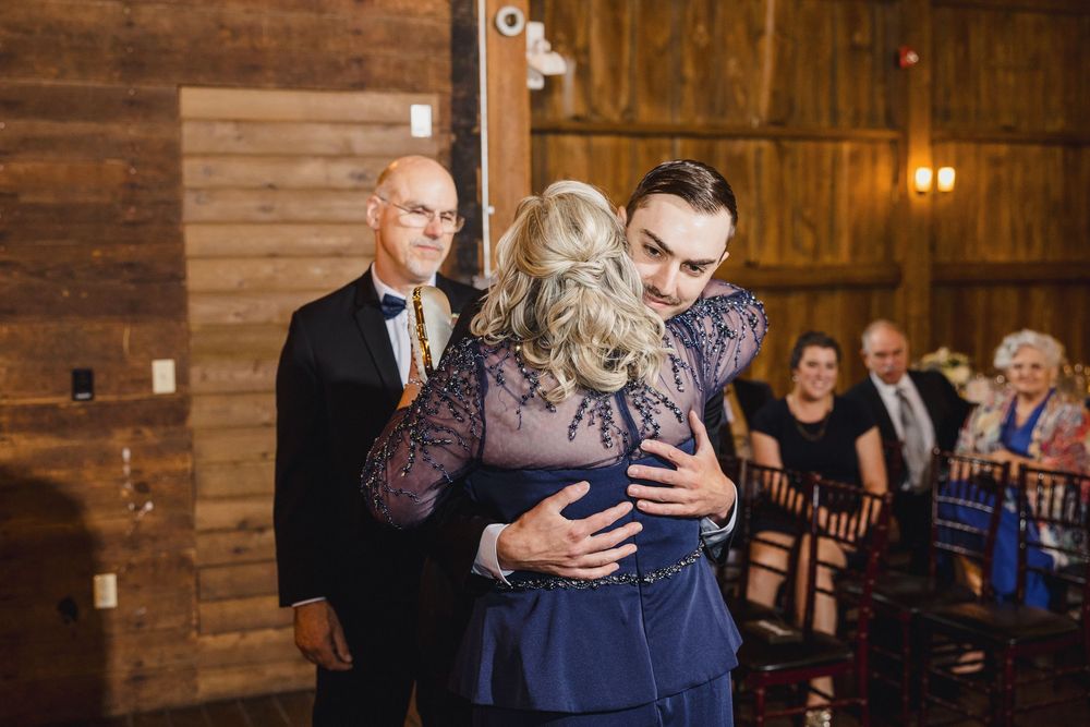 A tender embrace shared during a rustic barn wedding ceremony with wooden walls and warm lighting.