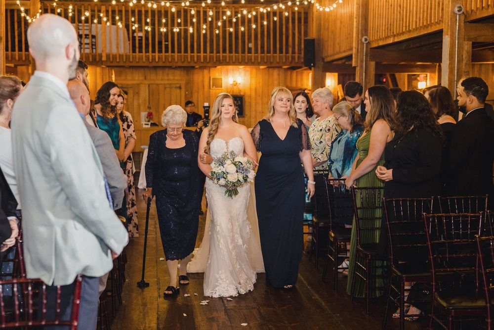 Wedding guests dance and celebrate under warm string lights in a rustic barn venue during an evening reception.