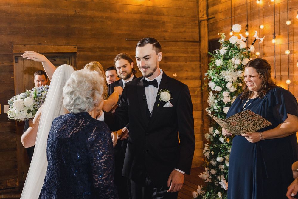Wedding guests dancing and celebrating on a rustic wooden dance floor with string lights overhead during reception.