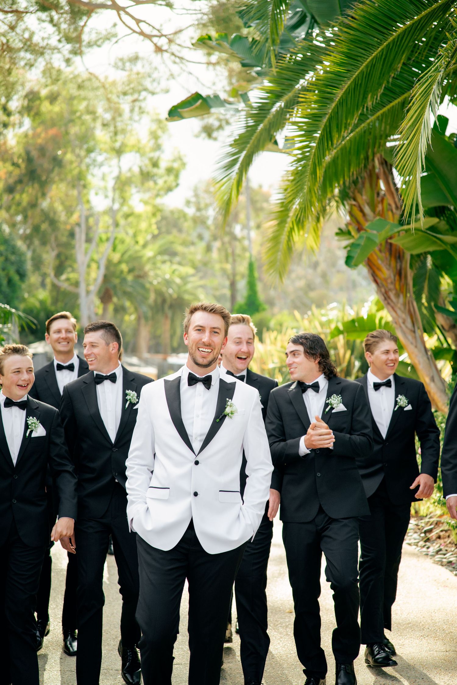 A bride with red hair in a light dress drinks from a glass on an outdoor patio overlooking a scenic coastal view.