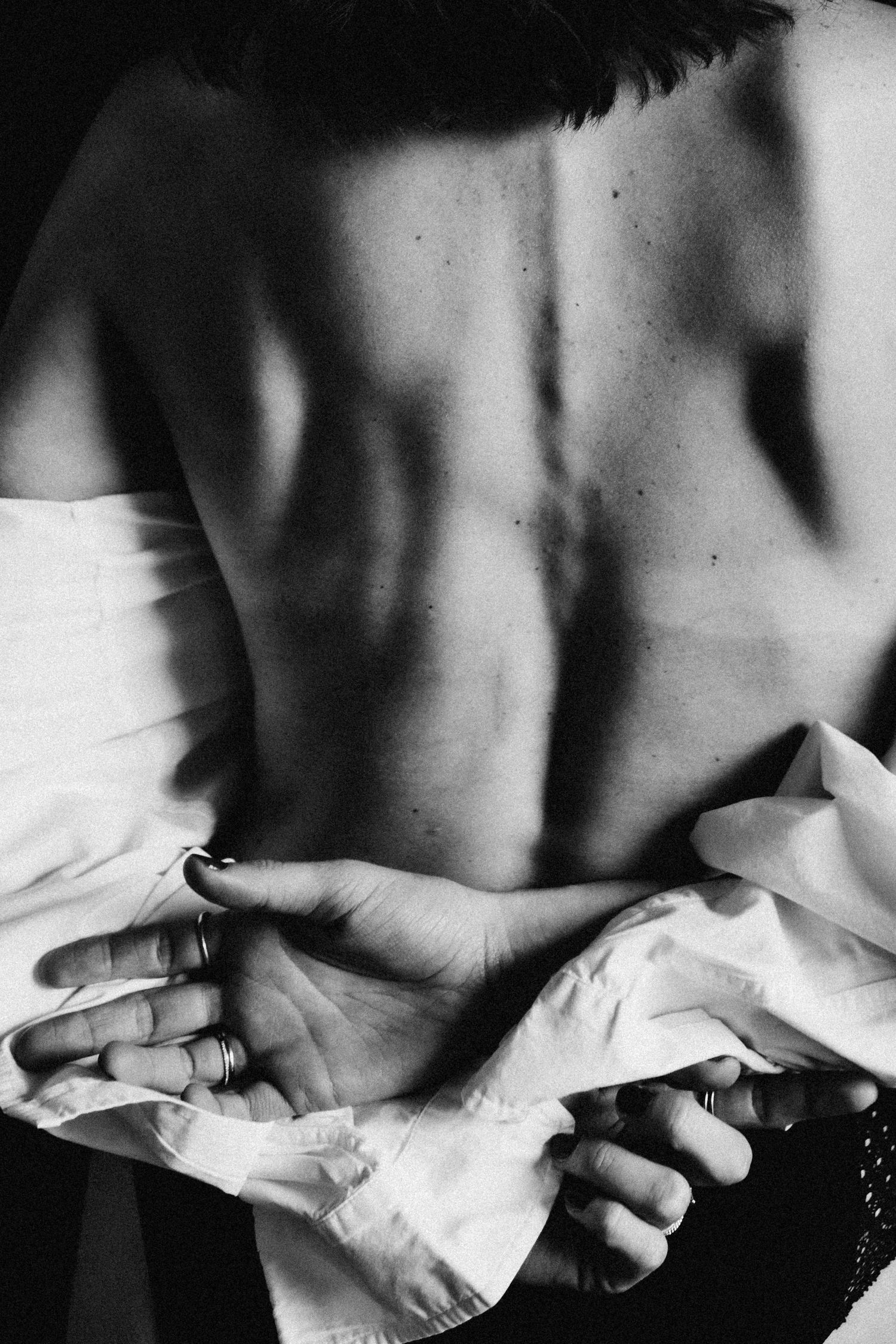 Black and white close-up of a woman holding a white shirt behind her bare back.