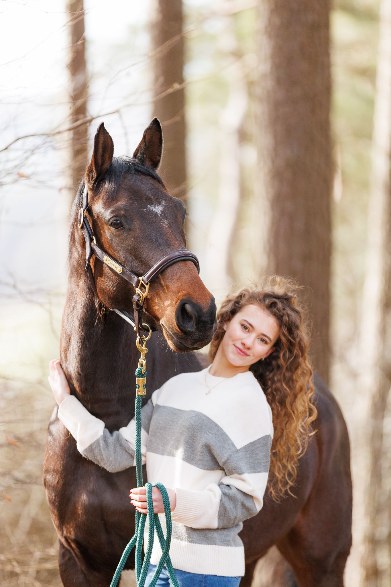 A person in a flowing red gown poses with a majestic black horse in an autumn forest setting.