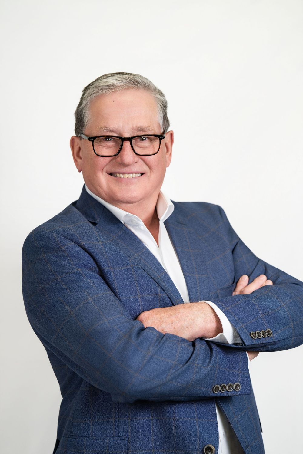 Professional headshot portrait of someone wearing a navy blue blazer, white shirt and glasses against white background.