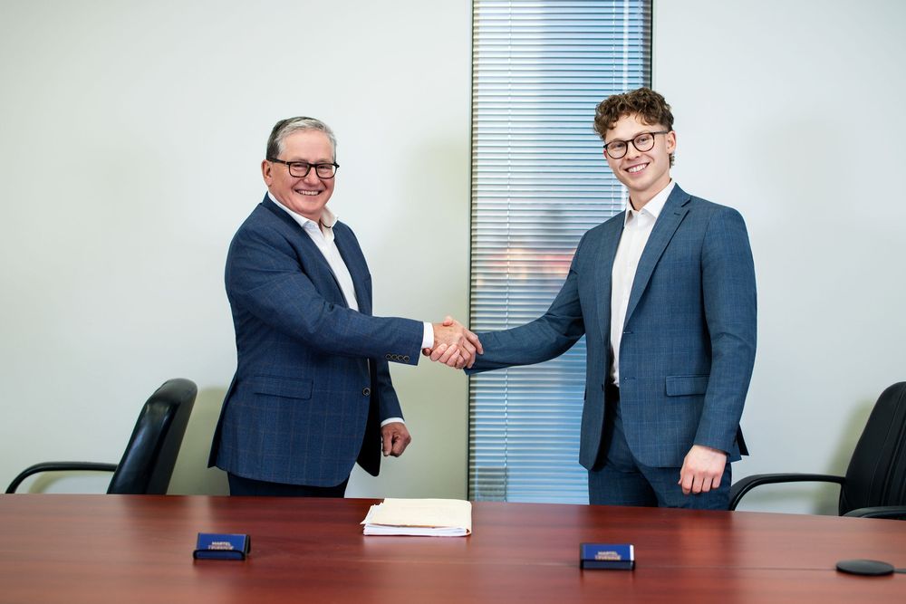 Two businesspeople shake hands in a professional office setting during a meeting.