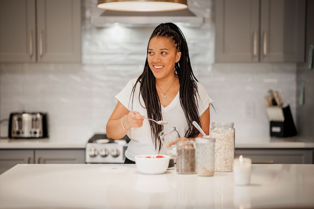 A person writing in a notebook at a white kitchen counter with glass jars nearby.