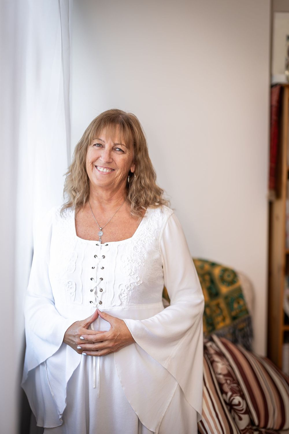 A person in a flowing white dress with bell sleeves poses against a light wall in a series of casual portraits.