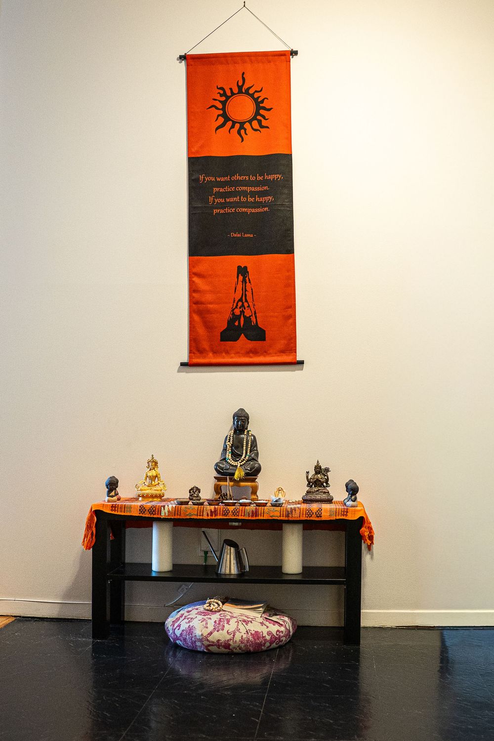 A meditation space with orange wall hangings and decorative Buddha statues displayed on a dark wooden bench.