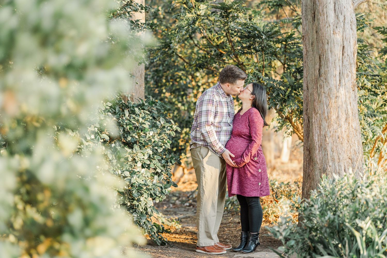 A couple shares a tender moment beneath a towering tree during a golden sunset engagement photoshoot.