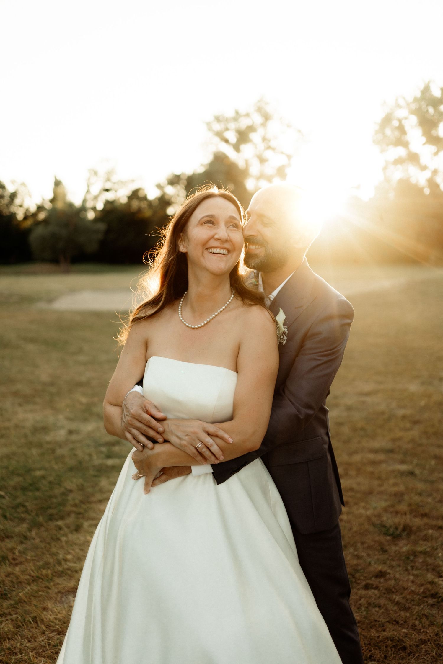 Newlywed couple embraces in golden sunlight during sunset outdoor wedding photoshoot.