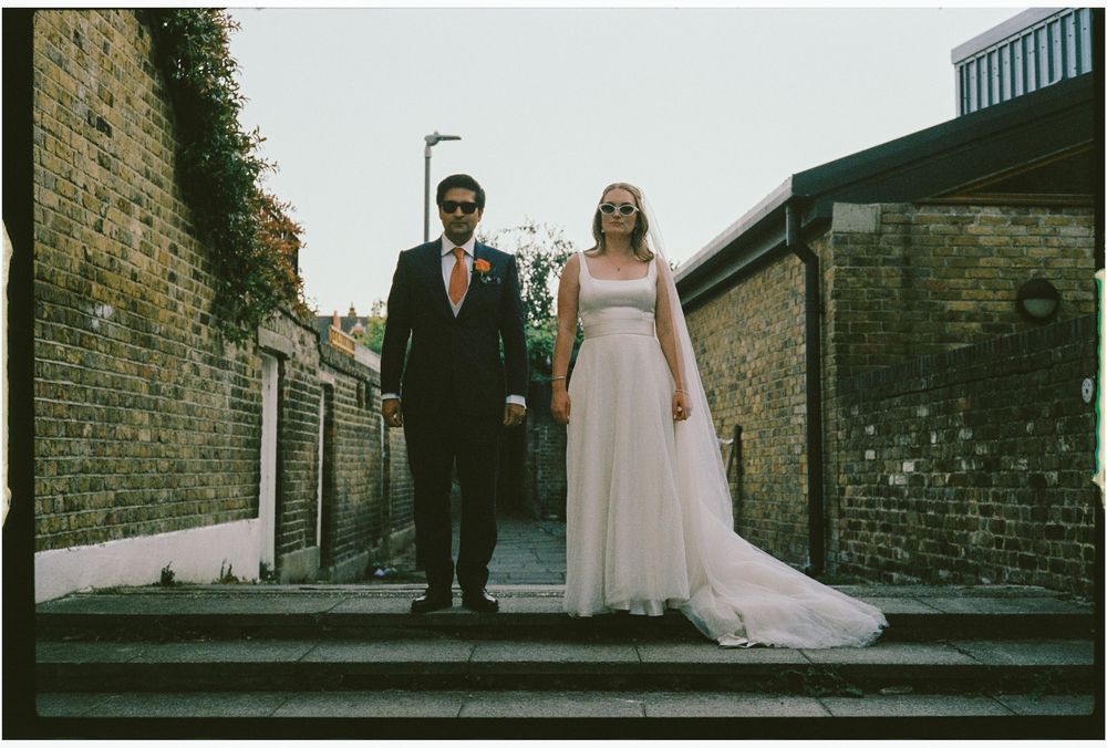 Couple in formal wedding attire walking down a cobblestone street in an urban setting.