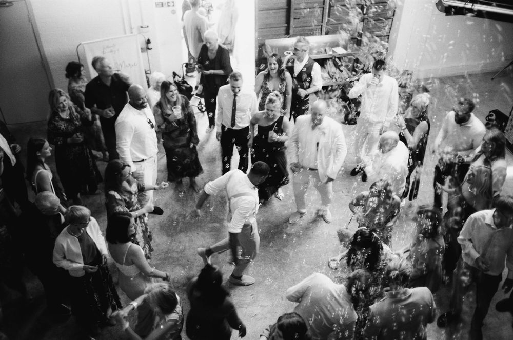 A black and white panoramic photo showing a crowd of people in white clothing mingling at an indoor event.
