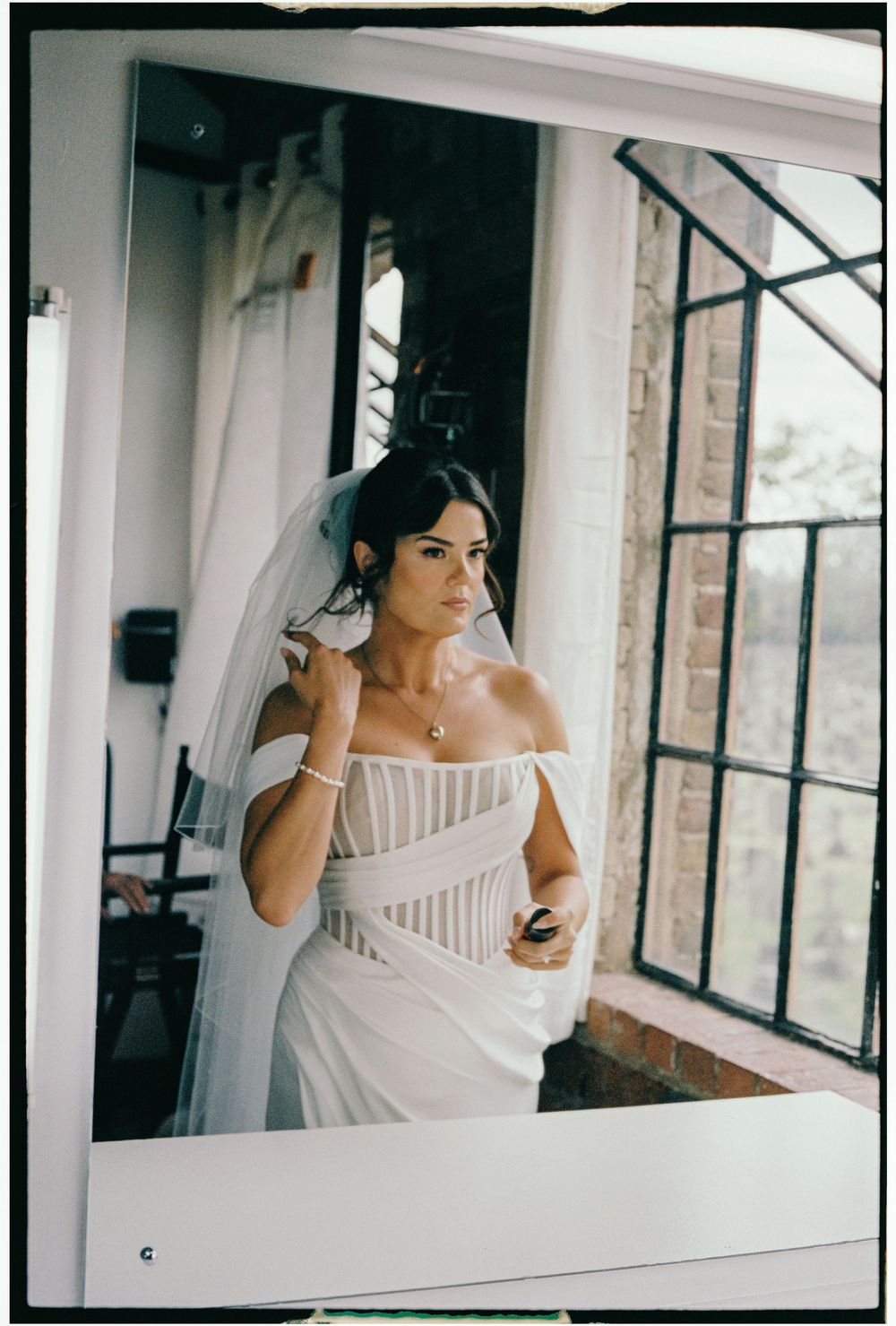 A person in a white off-shoulder dress gazes thoughtfully out a window in an elegant interior setting.