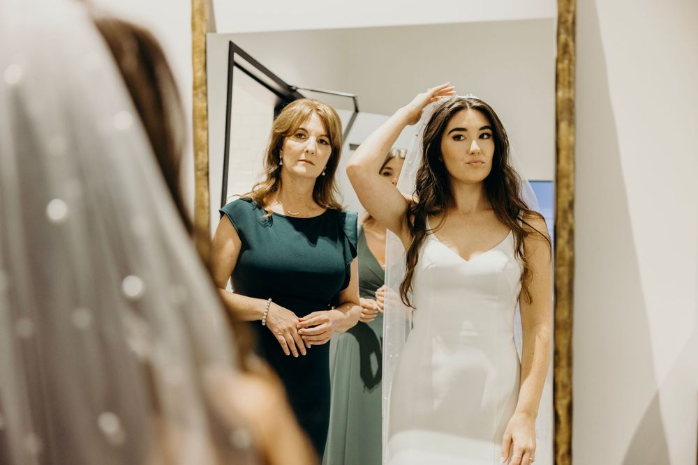 Woman in dark green dress stands in bridal shop looking at wedding gowns on display.