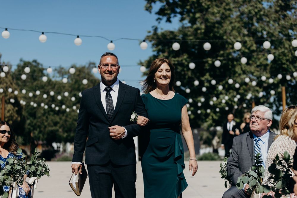 Wedding guests walk together on a sunny day with string lights and greenery decorating an outdoor venue.