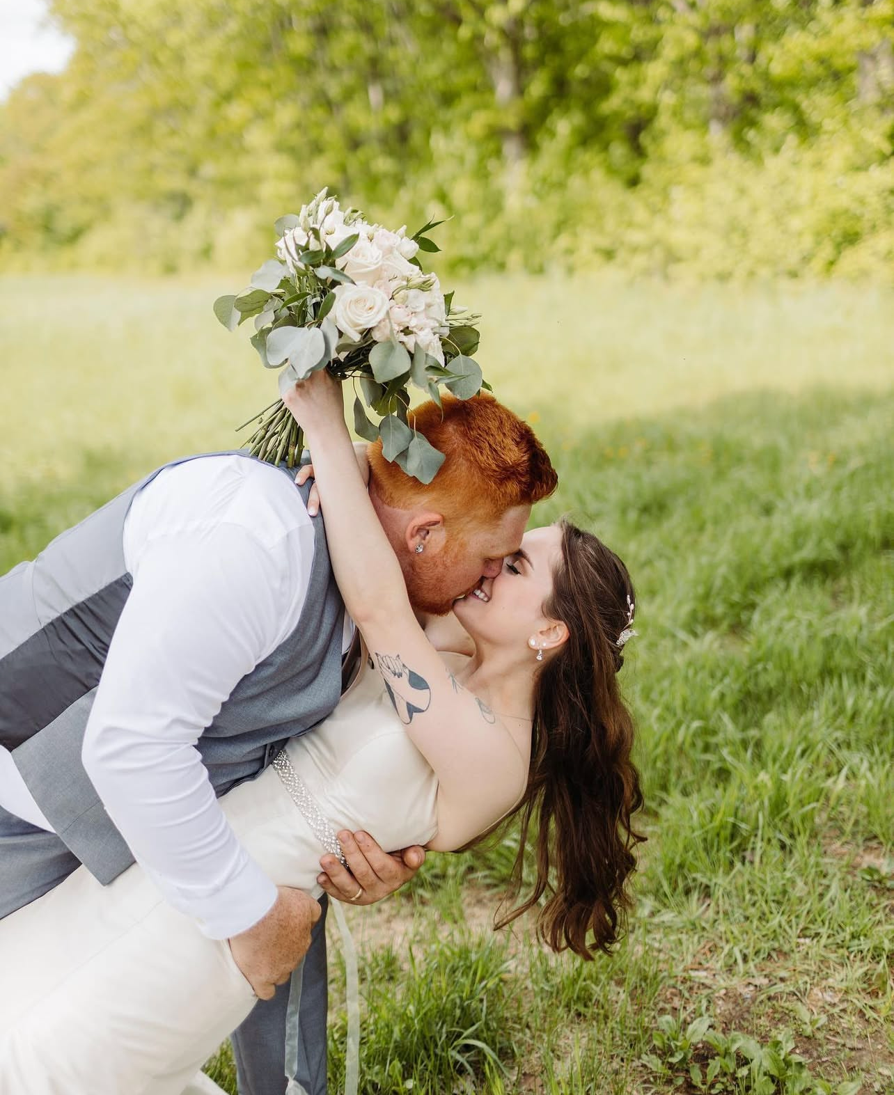 A couple in wedding attire shares romantic kisses in a grassy outdoor setting with soft natural lighting.