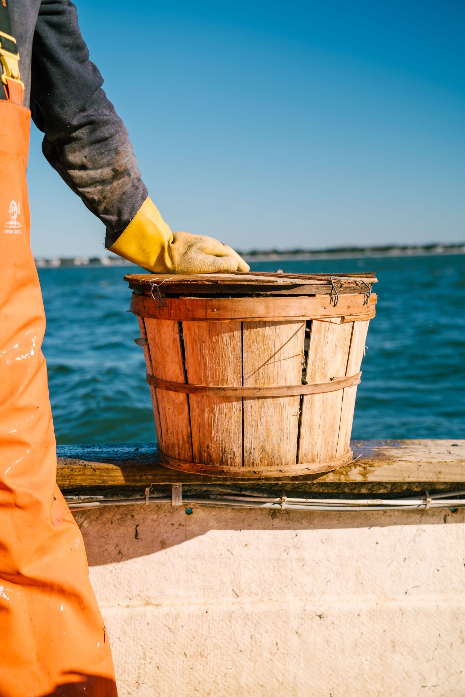 Wooden bushel baskets sit on a dock by bright blue water with orange safety equipment visible in frame.