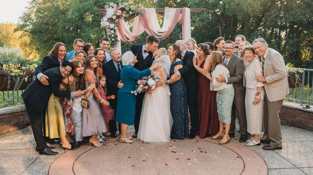 Wedding party poses together for panoramic group photos in an outdoor garden setting during golden hour.