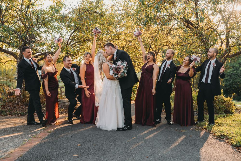 Wedding party celebrates outdoors with raised arms against golden autumn trees at sunset at the Atrium at Meadowlark Botanical Garden