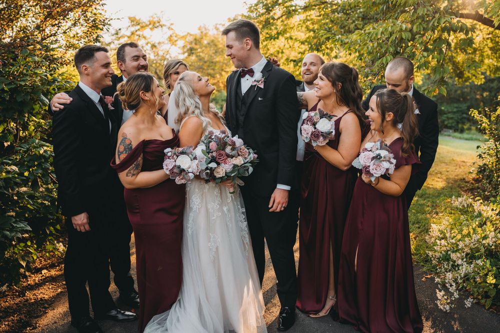 Wedding party shares joyful moment together in burgundy attire during golden hour at the Atrium at Meadowlark Botanical Garden