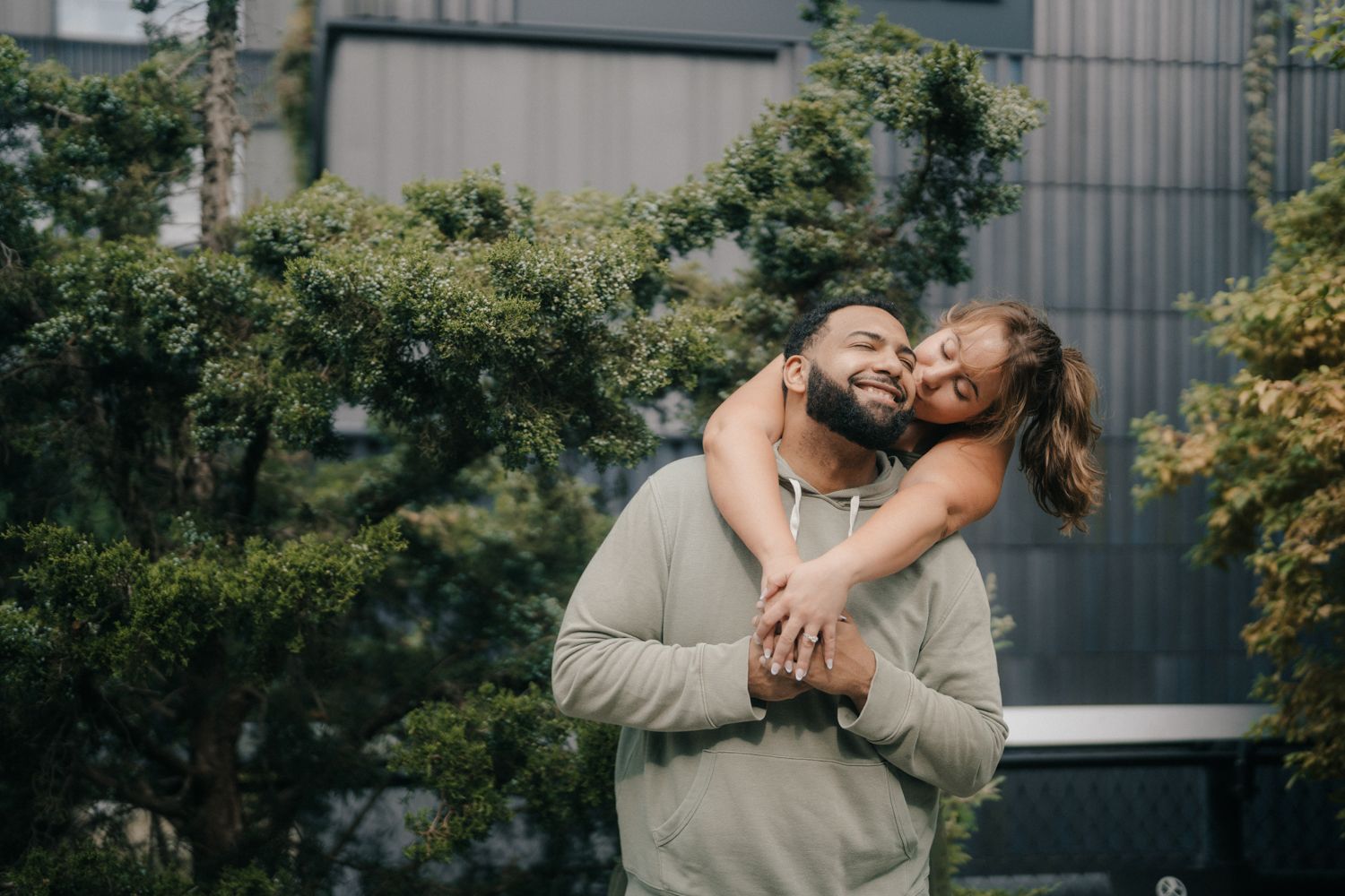 A couple shares a romantic moment while dancing together outdoors near a modern building and garden setting.