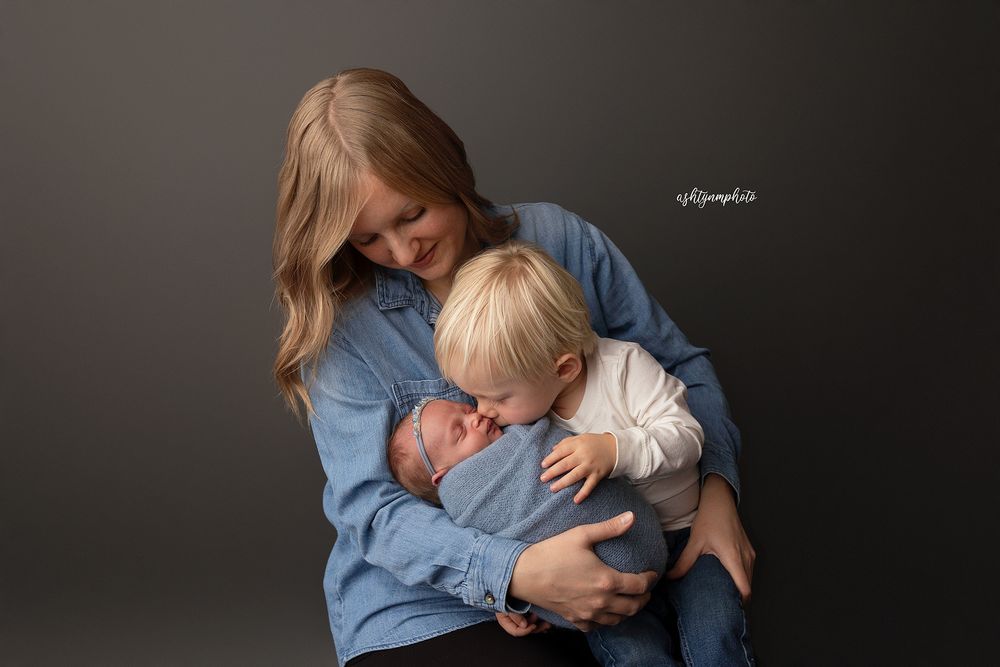Intimate studio portrait of mother and child embracing against dark grey background.