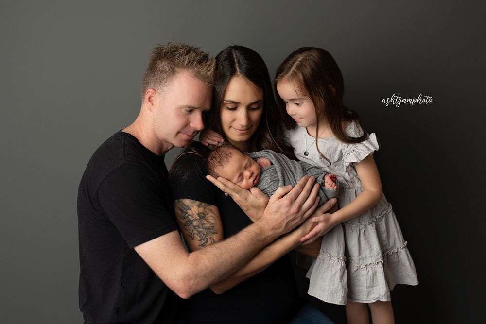 Studio portrait of family in black and grey tones sharing tender moment against dark background.