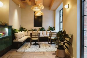 Modern cozy lounge area with beige sectional sofa, hanging pendant lights, and potted plants against green accent wall.