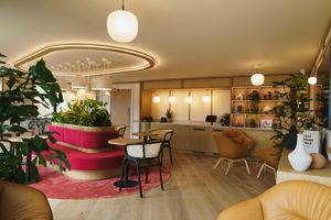 Modern office interior with hanging pendant lights, beige tones, and comfortable seating areas creates a warm welcoming atmosphere.