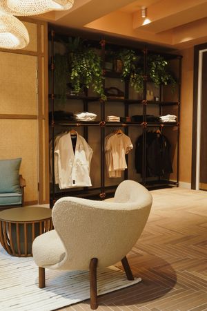 Modern retail space with white armchair and clothing rack display adorned with hanging plants and crystal chandeliers.
