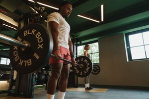 Athletic person lifting weights with black barbell plates in a well-lit modern gym facility.