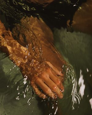 Feet splashing in dark water creating ripples and movement against a moody green background.
