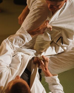 Two martial artists in white gis practicing grappling techniques on a training mat.