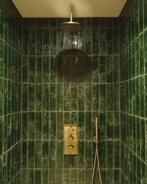 Luxurious green marble bathroom with vertical tiling and gold fixtures illuminated by ceiling lighting.