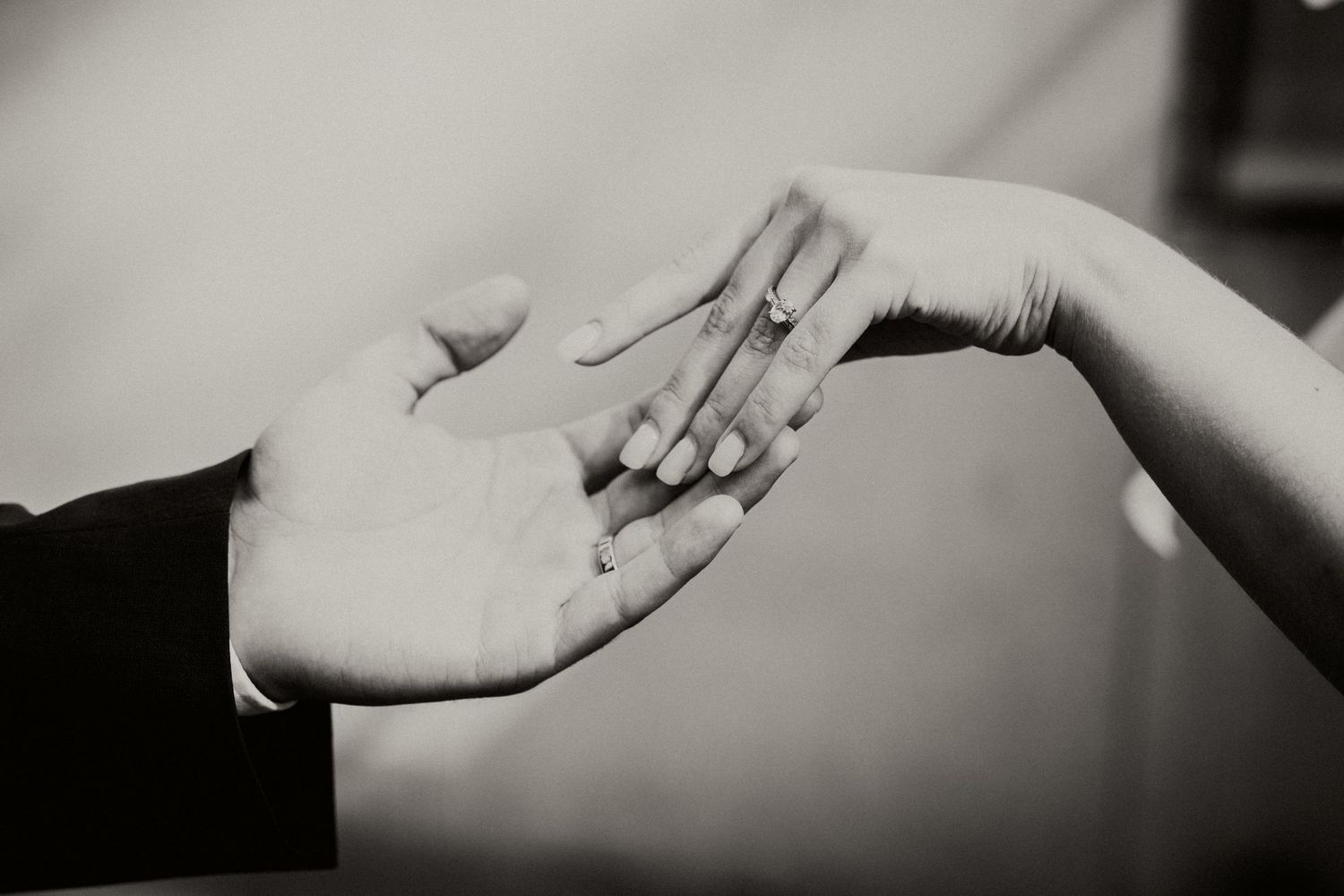 Black and white artistic close-up of hands reaching toward each other.