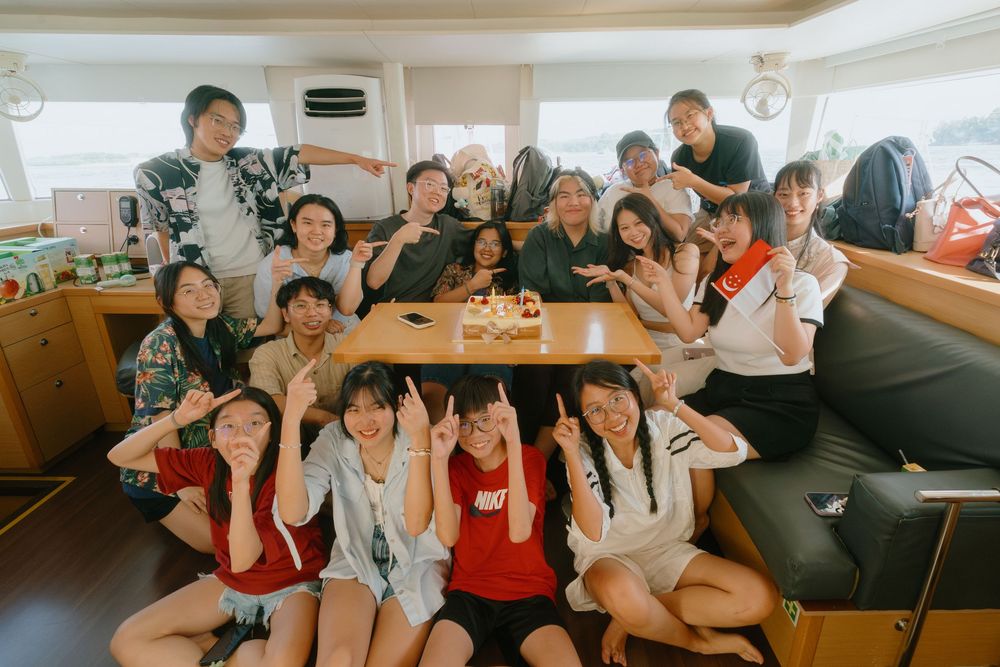 A group of friends gather together inside a boat cabin, posing cheerfully around a table.