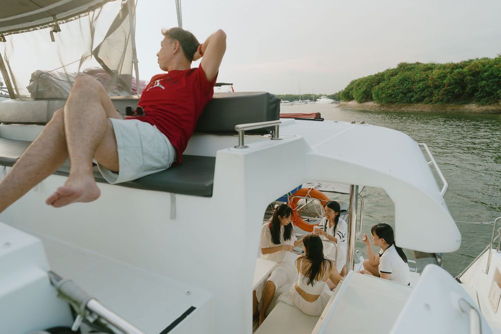 Passengers relaxing on a white boat deck while cruising along a scenic waterway bordered by green foliage.